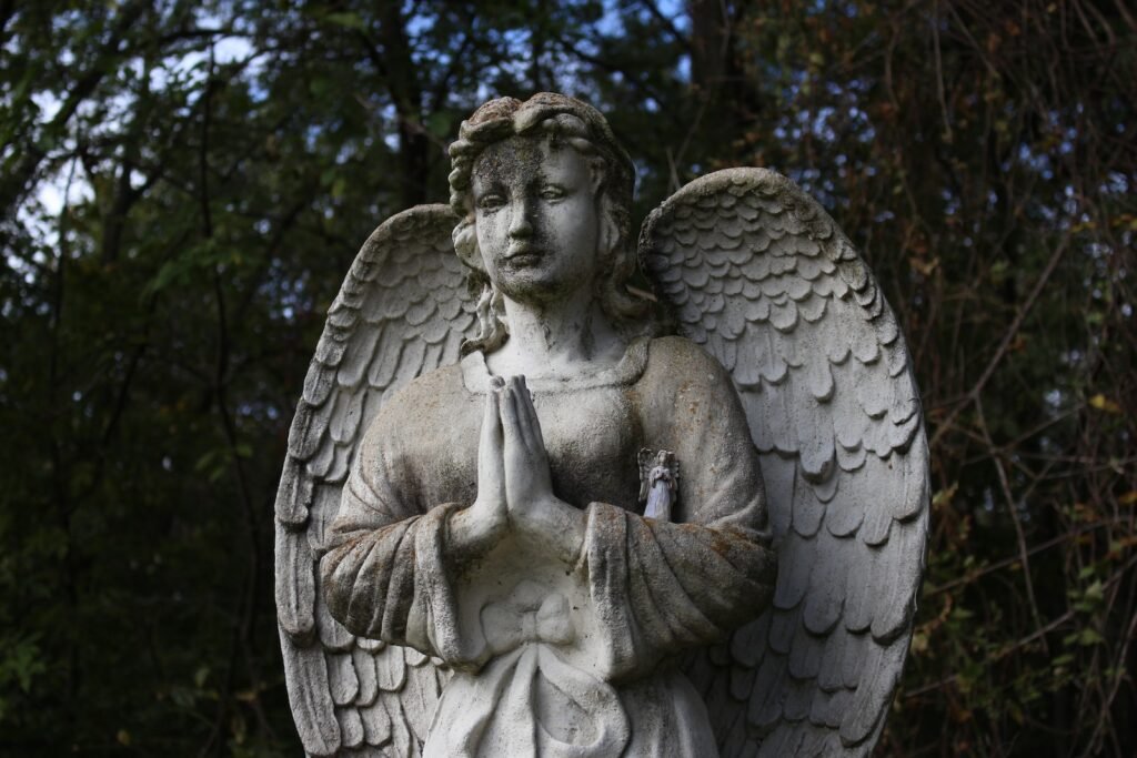 angel statue under green tree during daytime